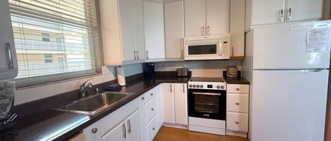 A compact kitchen with white cabinets, a stainless steel sink, a microwave, an oven, and a white refrigerator.