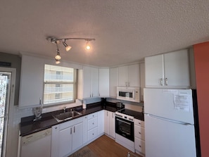 A compact kitchen with white cabinets, a microwave, a stove, and a refrigerator.
