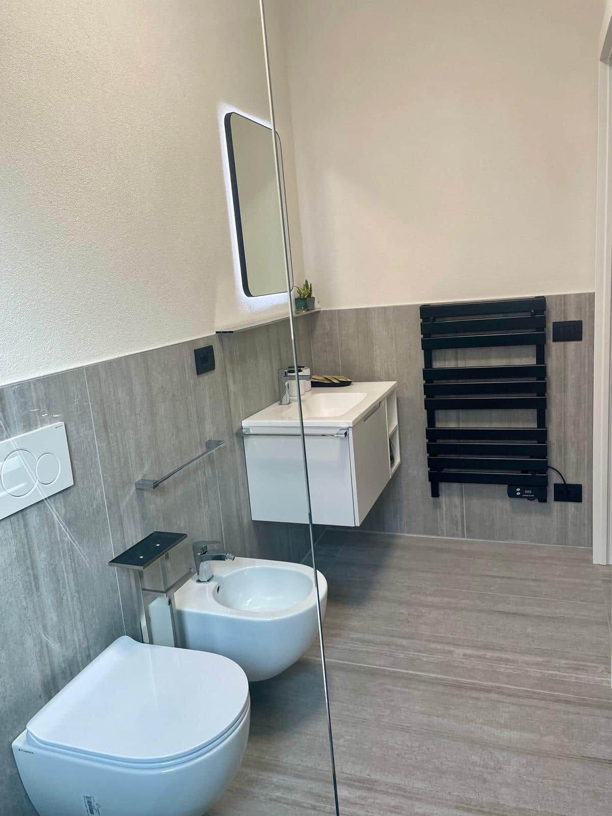 Un bagno moderno con servizi igienici, bidet e lavandino. È presente un porta asciugamani e uno specchio a parete.