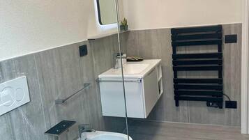 Un bagno moderno con servizi igienici, bidet e lavandino. È presente un porta asciugamani e uno specchio a parete.