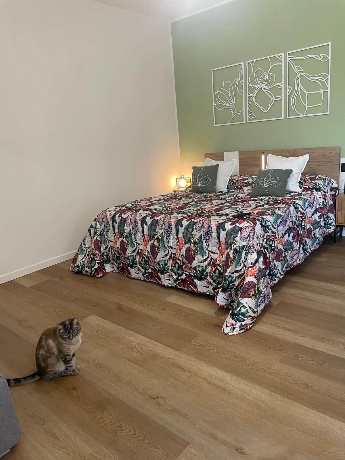 Ein Schlafzimmer mit floralem Bettbezug, einer Katze auf dem Boden und Wandbildern.