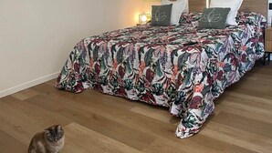 Een slaapkamer met een bloemenbedekking, een kat op de vloer en wanddecoratie.