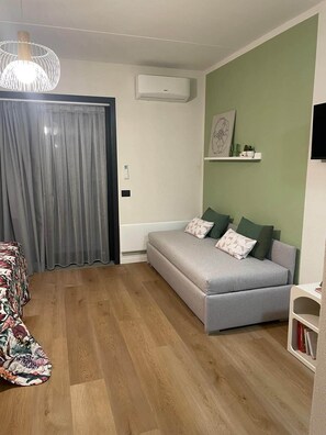 Una sala moderna con un sofá gris, un sillón estampado, suelo de madera, una lámpara colgante y un aire acondicionado de pared.
