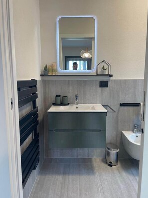 Un baño moderno con un espejo grande, un tocador con lavabo y un lavamanos independiente.