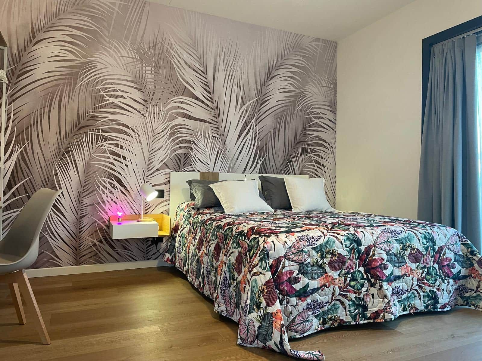 A bedroom with a bed, a nightstand, a chair, and a wall with a leaf pattern.