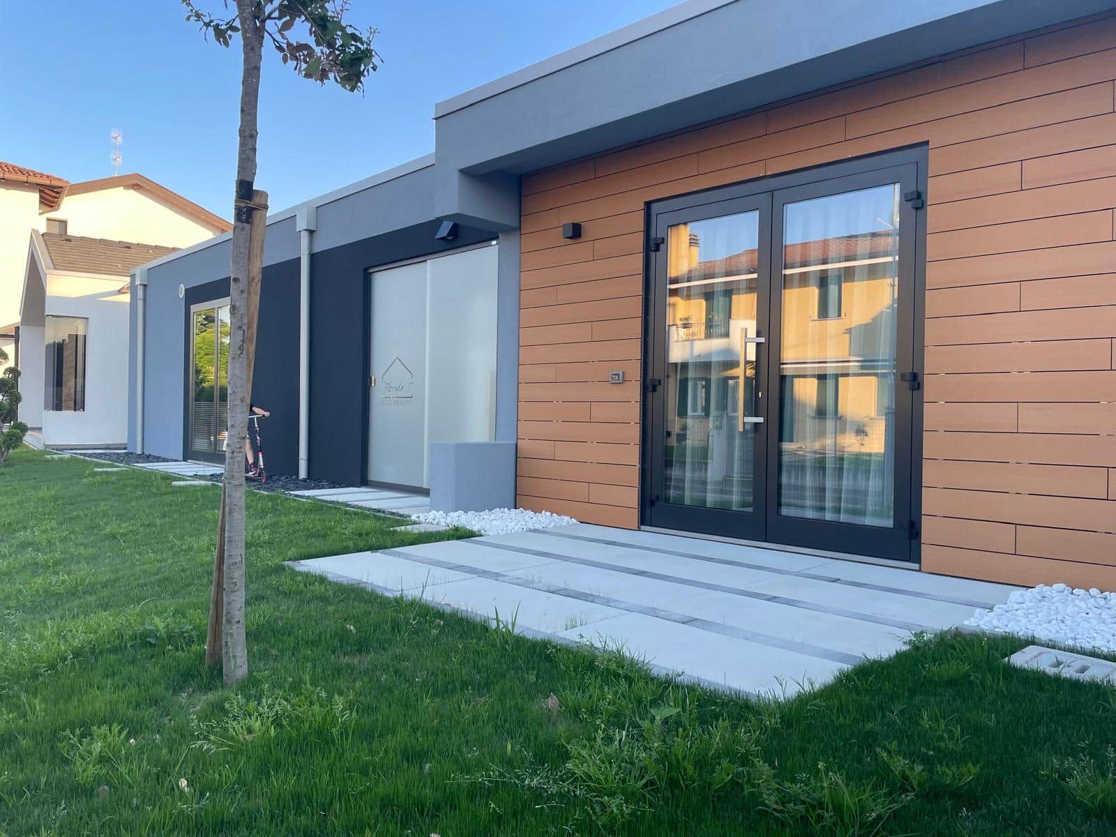 A modern residential building with a flat roof, large sliding glass doors, and a well-maintained lawn.