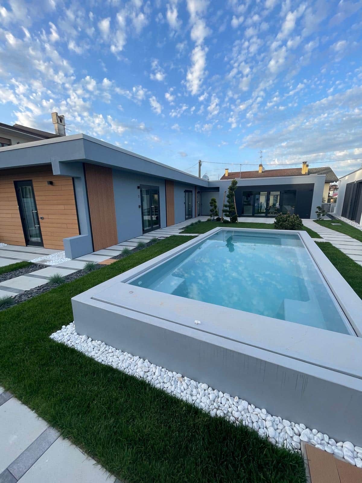 Une maison moderne avec une piscine, une pelouse bien entretenue et un ciel dégagé.