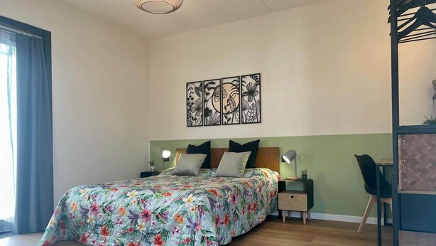 Een slaapkamer met een bed, nachtkastjes, een kunstwerk aan de muur en een stoel.