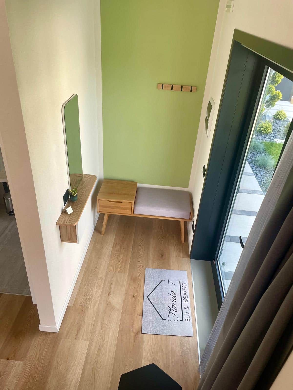 Ein Zimmer mit einer Holzbank, einem kleinen Tisch, einem Spiegel und einer zur Außenseite führenden Tür.