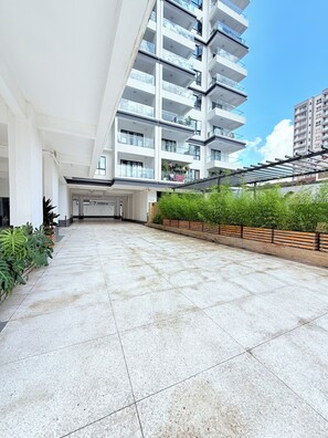 A spacious indoor area with a tiled floor, a modern building with balconies, and a row of potted plants. - Stylish Kilimani 2BR with Pool, Wi-Fi and Free Parking near Yaya Centre (Nairobi)