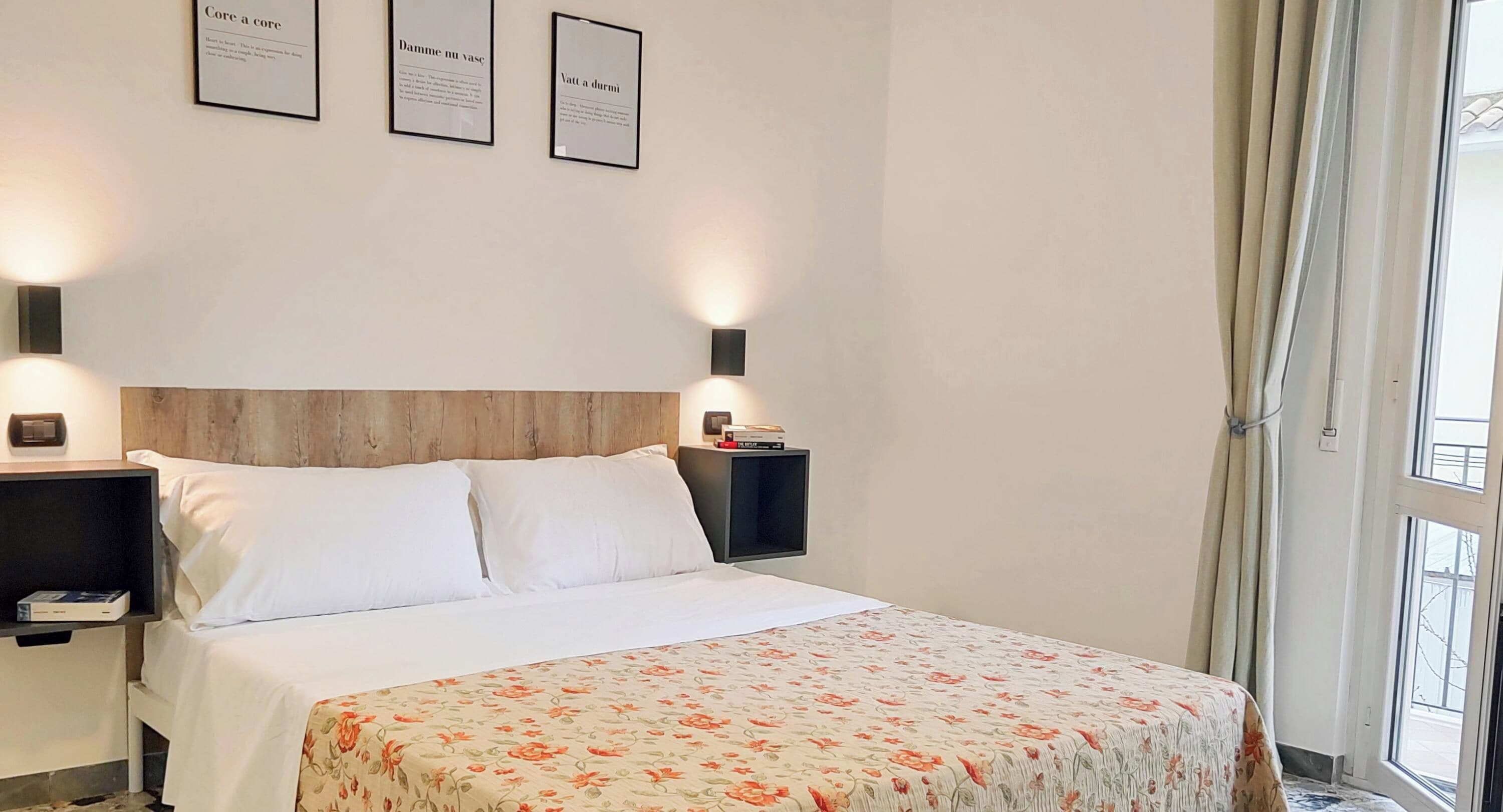A hotel room with a bed, two bedside tables, and three framed quotes on the wall.
