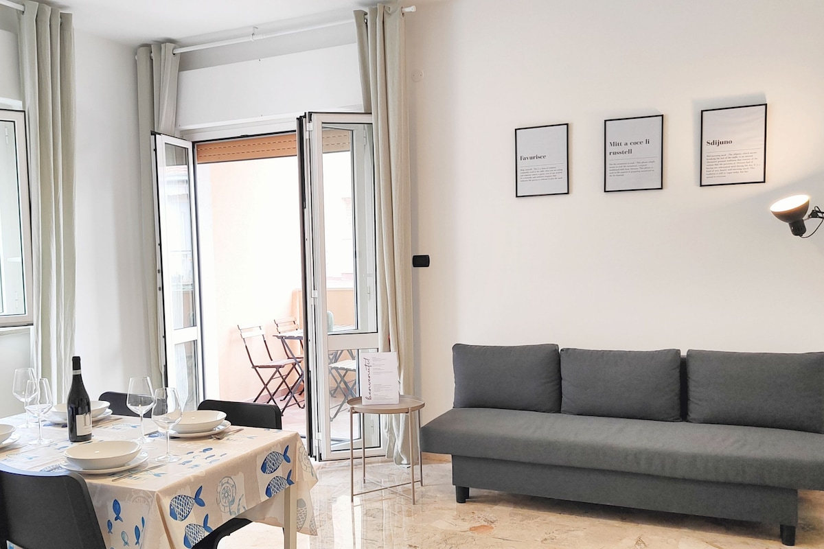 A modern living room with a grey sofa, a dining table set with plates and wine glasses, and a small side table.