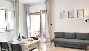 Ein modernes Wohnzimmer mit einem grauen Sofa, einem Esstisch gedeckt mit Tellern und Weingläsern sowie einem kleinen Beistelltisch.