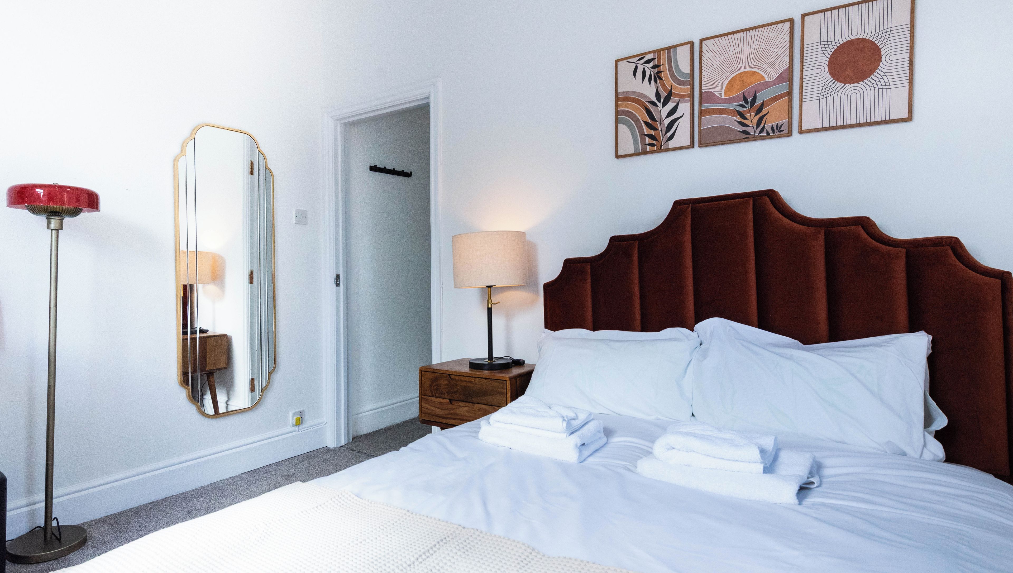 Een hotelkamer met een bed, nachtkastje, lamp, spiegel en kunst aan de muur.