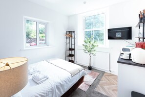A modern bedroom with a bed, a bedside lamp, a plant, a radiator, and a television. - The Stanley Arms Hotel by Guestz (Seascale)