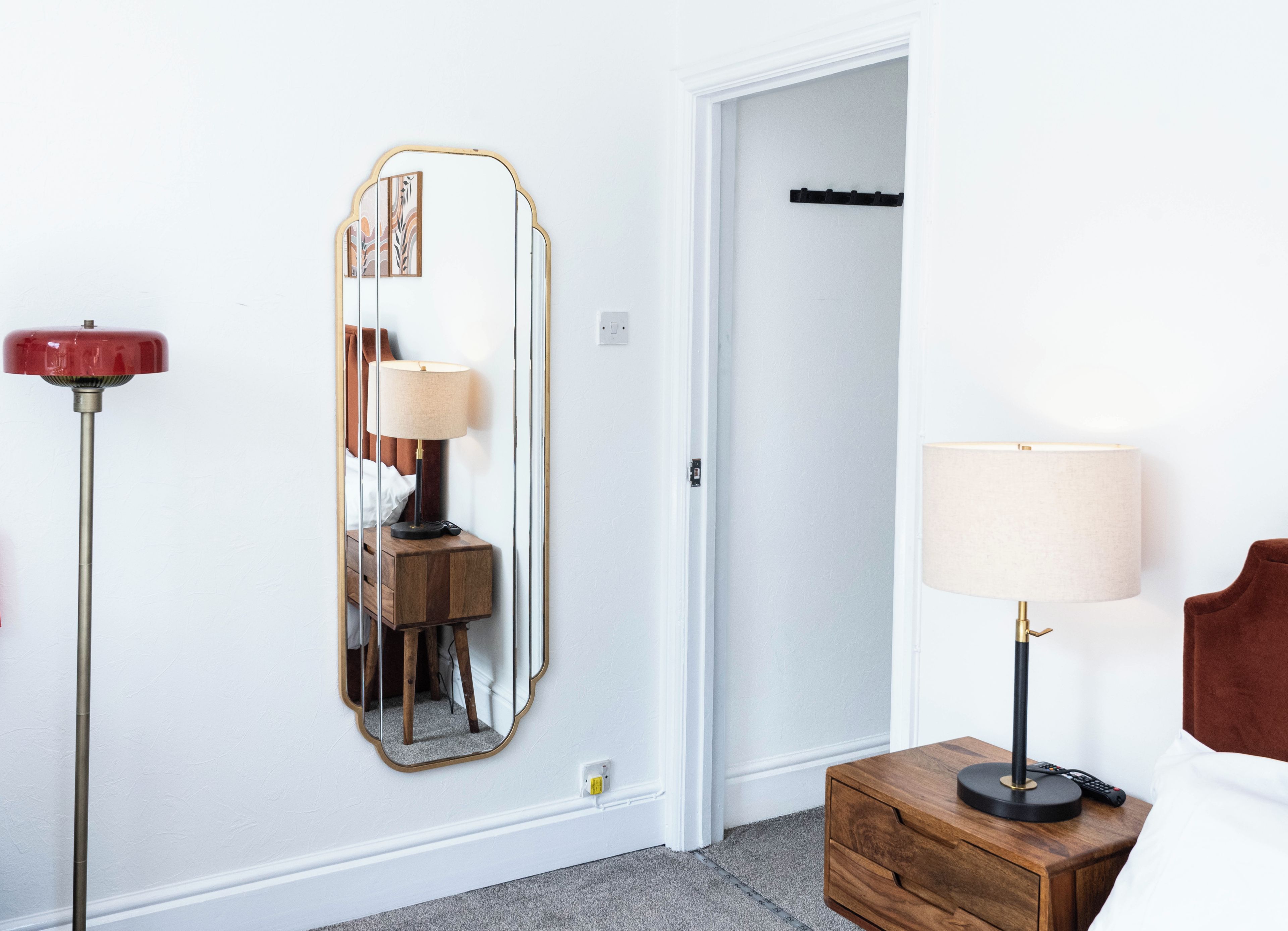Une chambre d’hôtel avec une table de chevet en bois, un miroir, une lampe sur pied et un lit.