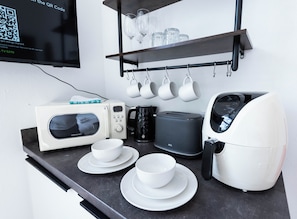 A kitchenette with a microwave, toaster, coffee maker, and a shelf with cups and glasses.