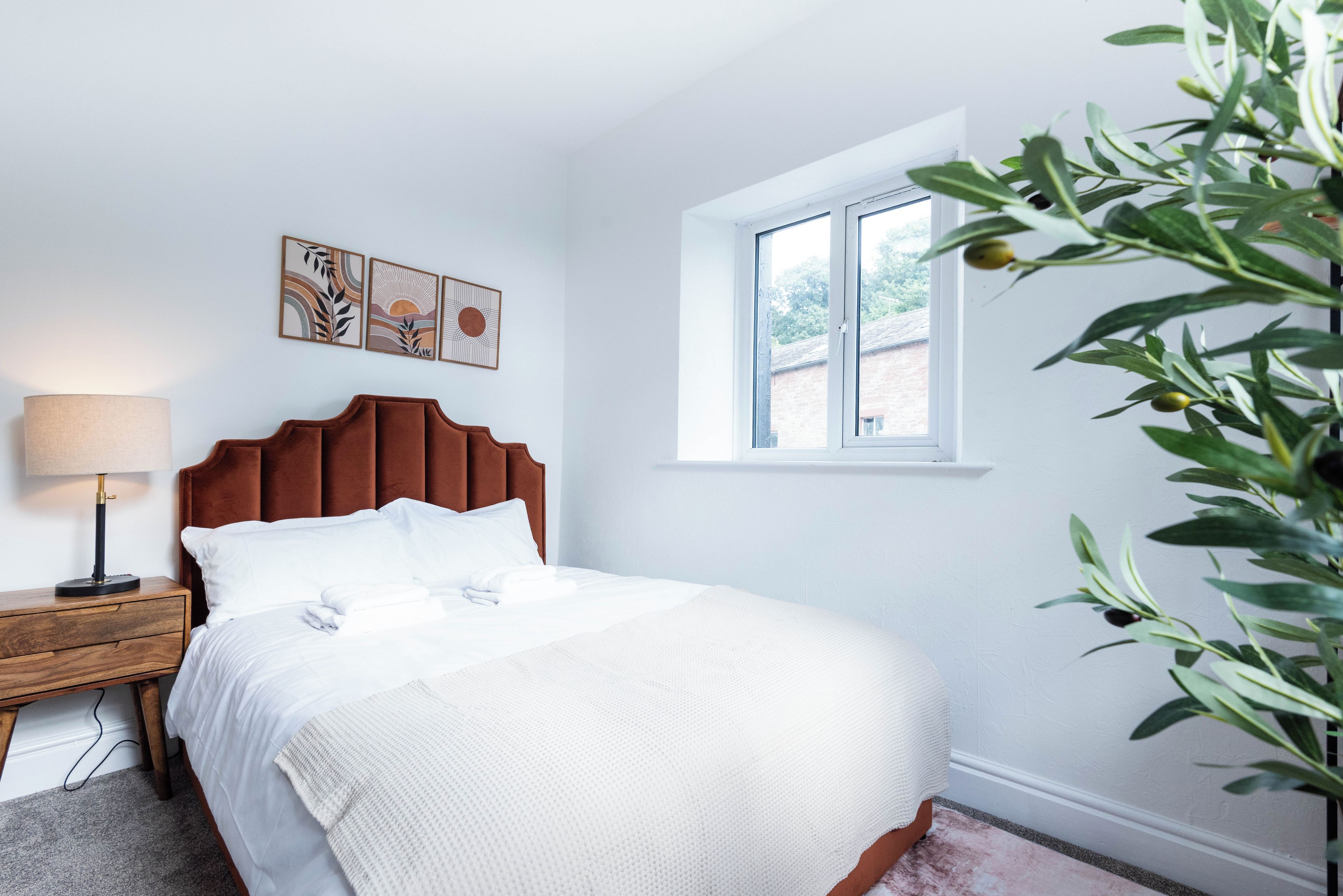 A bedroom with a bed, a nightstand, a lamp, a window, and wall art.