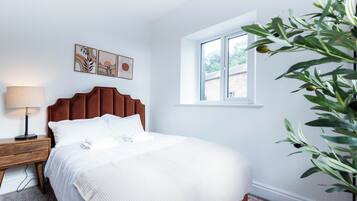 A bedroom with a bed, a nightstand, a lamp, a window, and wall art.