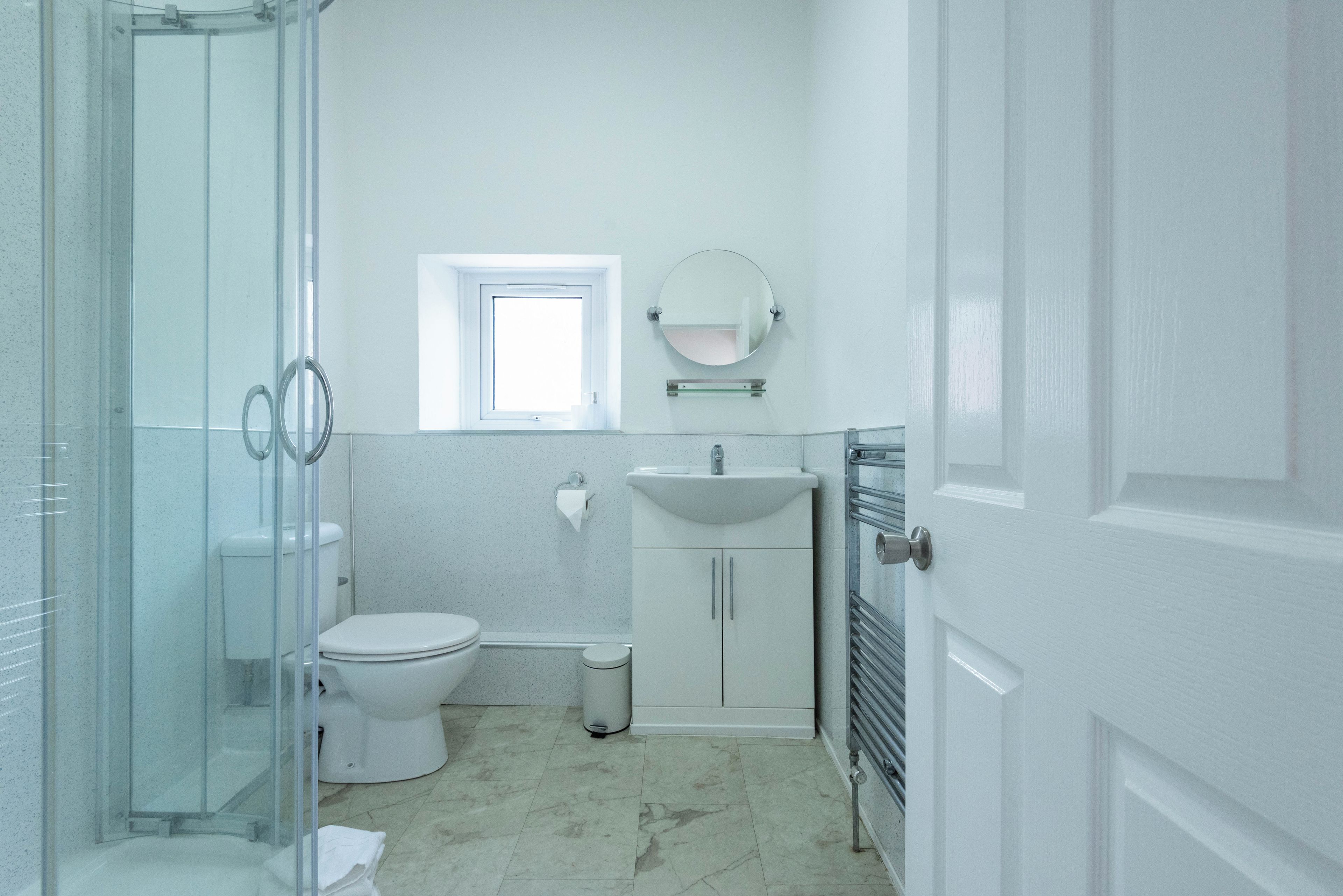 A bathroom with a glass shower enclosure, a toilet, a sink, and a mirror.