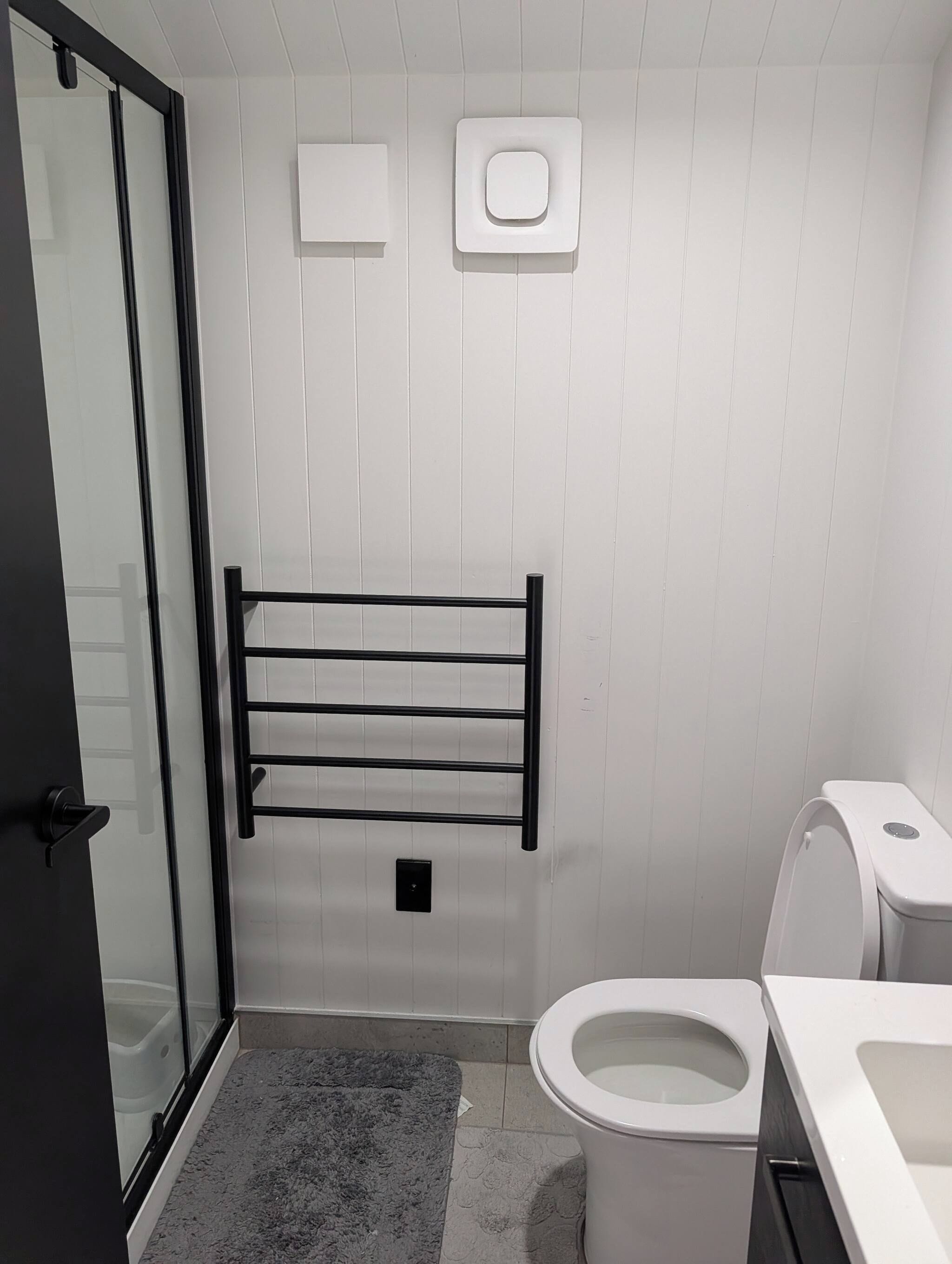 Kylpyhuone, jossa on wc, pyyhekoukku, lasinen suihkuseinä ja valkoinen pesuallas.