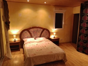 Ein Schlafzimmer mit einem hölzernen Bett, zwei Nachttischen mit Lampen, einem Fenster und einer Tür.