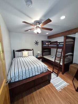 Une chambre avec un lit simple, un lit superposé, un ventilateur de plafond et une table de chevet avec une lampe.