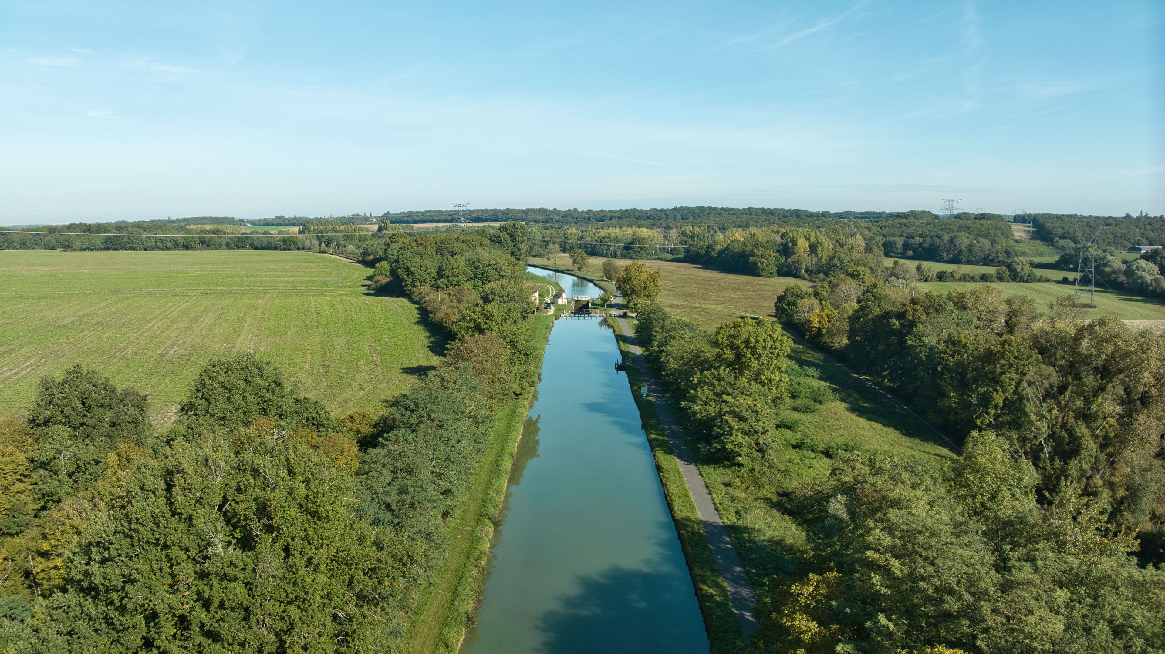 Eine Luftaufnahme eines Flusses mit einer Brücke, umgeben von grünen Feldern und Bäumen.