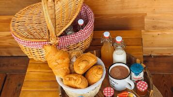 A wooden table with a wicker basket containing croissants, a bottle of milk, a mug of coffee, and bowls of fruit.