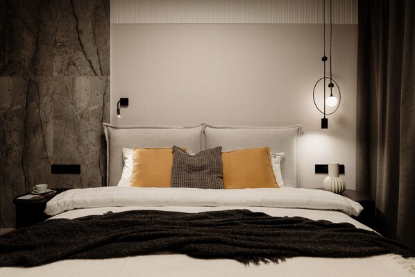 A modern bedroom with a stone wall, a bed with multiple pillows, a bedside table with a lamp, and a hanging light fixture.