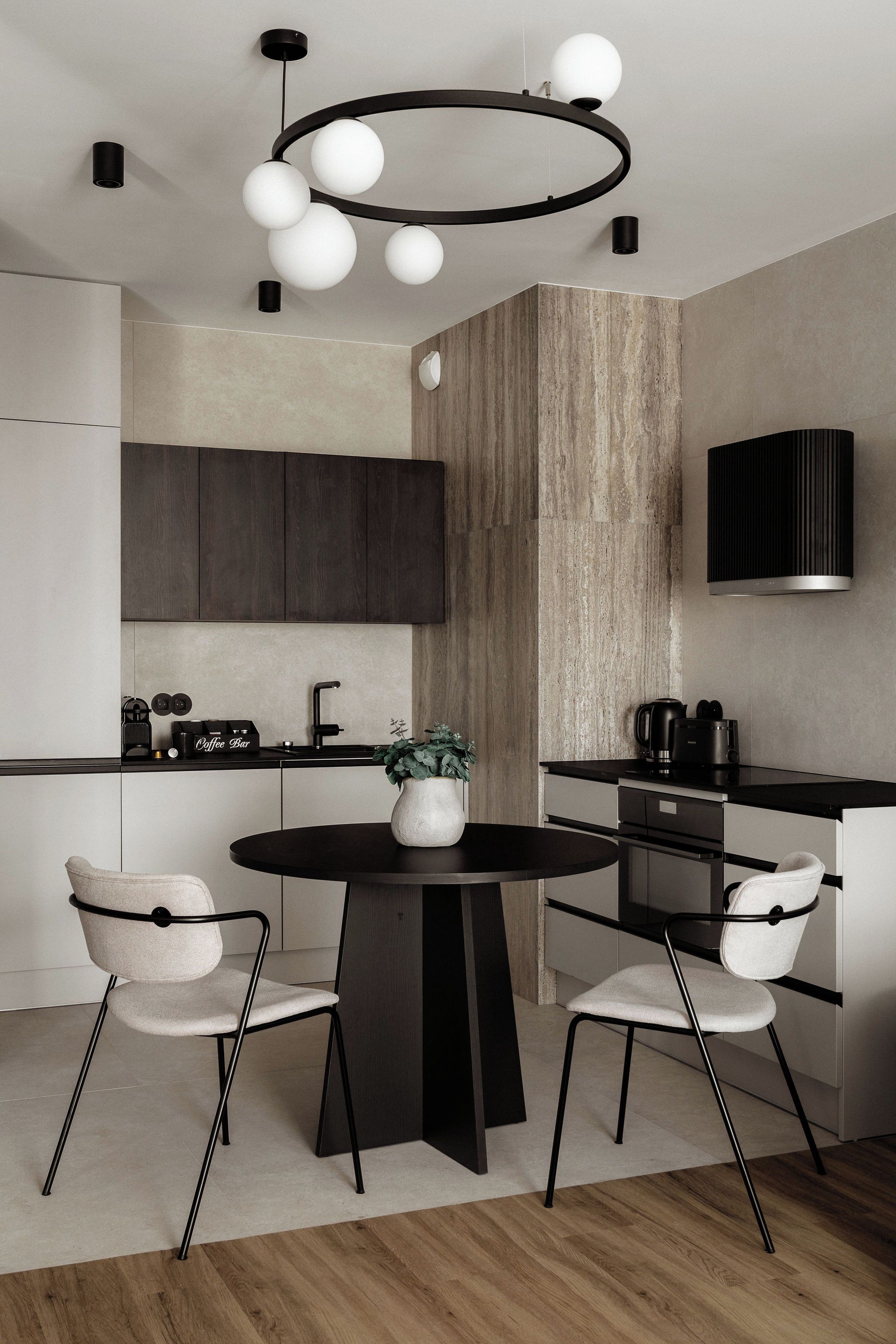 A modern kitchen with a round dining table, two chairs, a coffee bar, and a built-in stove.