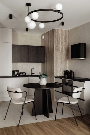 A modern kitchen with a round dining table, two chairs, a coffee bar, and a built-in stove.