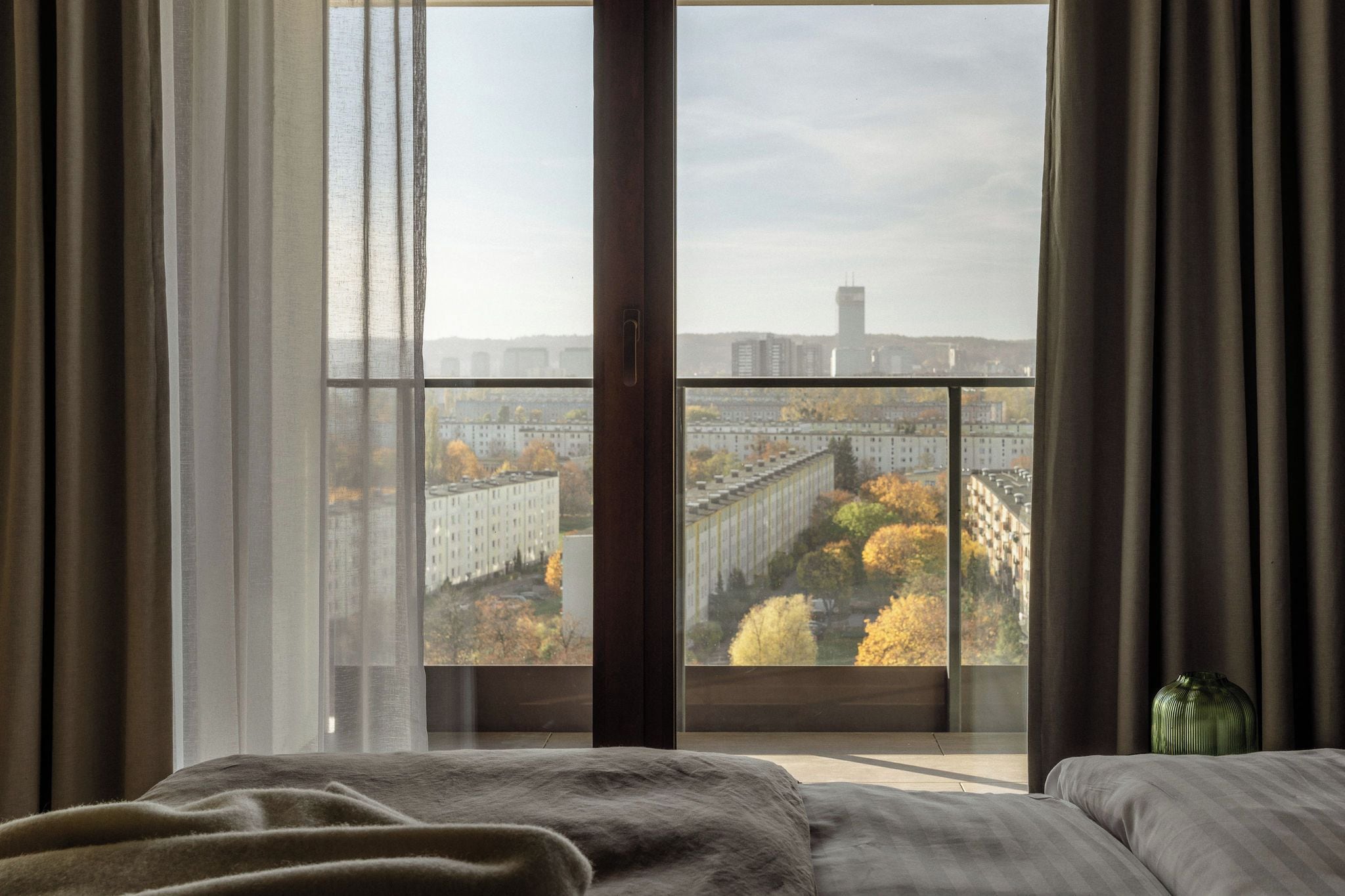 A bedroom with a large window, a bed, and a vase.