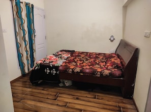 A small room with a wooden floor, a bed with a floral bedspread, a curtain with a wavy pattern, and a white door. - VISA HOMESTAY
Private Cottage @ Your Budget
family-friendly and pet-friendly (Kodaikanal)