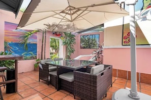 Eine Terrasse mit Korbmöbeln, einem Glastisch und einem großen Sonnenschirm.