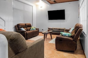 Ein Wohnzimmer mit einer Couch, Sesseln, einem Couchtisch und einem an der Wand befestigten Flachbildfernseher.