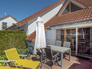A patio with a table and chairs, a white umbrella, and a view of a neighboring building. - 7a/t5 in the Holiday Apartment Park "freesenbruch" (Zingst)