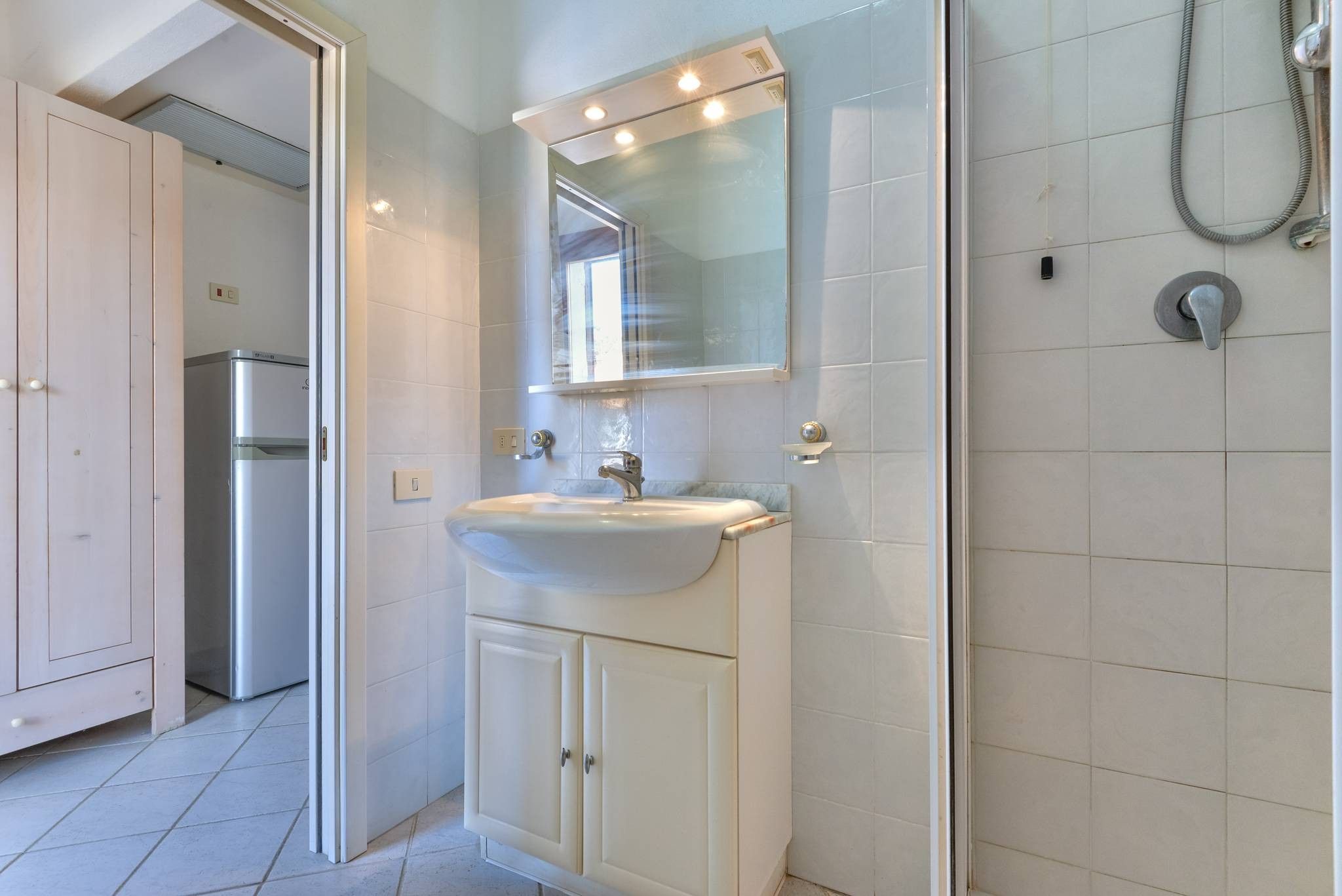 A bathroom with a sink, mirror, shower, and cabinets.