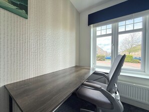 A conference room with a long table, a single office chair, and a window with a view of buildings and a tree.