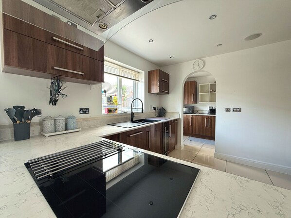 A modern kitchen with a black stove, wooden cabinets, and a window with blinds.