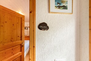 A wooden door leading to a room with a bed and a framed picture on the wall.