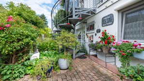 Een binnenplaats met een trap naar een balkon, omgeven door weelderige begroeiing en potplanten.