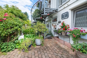 A courtyard with a staircase leading to a balcony, surrounded by lush greenery and potted plants. - Studio Apartment 'Röschen' with Shared Garden and Wi-Fi (Kirn)