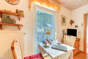 A cozy room with a table set for two, a wicker chair, a bookshelf, and a window with lace curtains. - Studio Apartment 'Röschen' with Shared Garden and Wi-Fi (Kirn)
