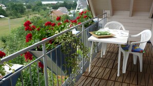 Een balkon met een tafel en stoelen, omgeven door groen en bloemen.