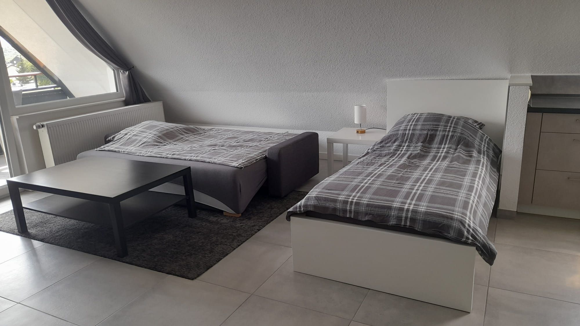 Ein modernes, kleines Zimmer mit einem Bett, einem kleinen Tisch und einem Nachttisch.