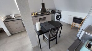 A compact kitchen with a washing machine, a dining table with chairs, and a small seating area.