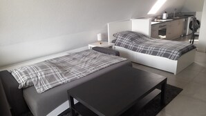 A modern bedroom with two beds, a small table, and a kitchenette in the corner. - Beautiful 1-bedroom apartment in charming Winden perfect for relaxing (Winden)