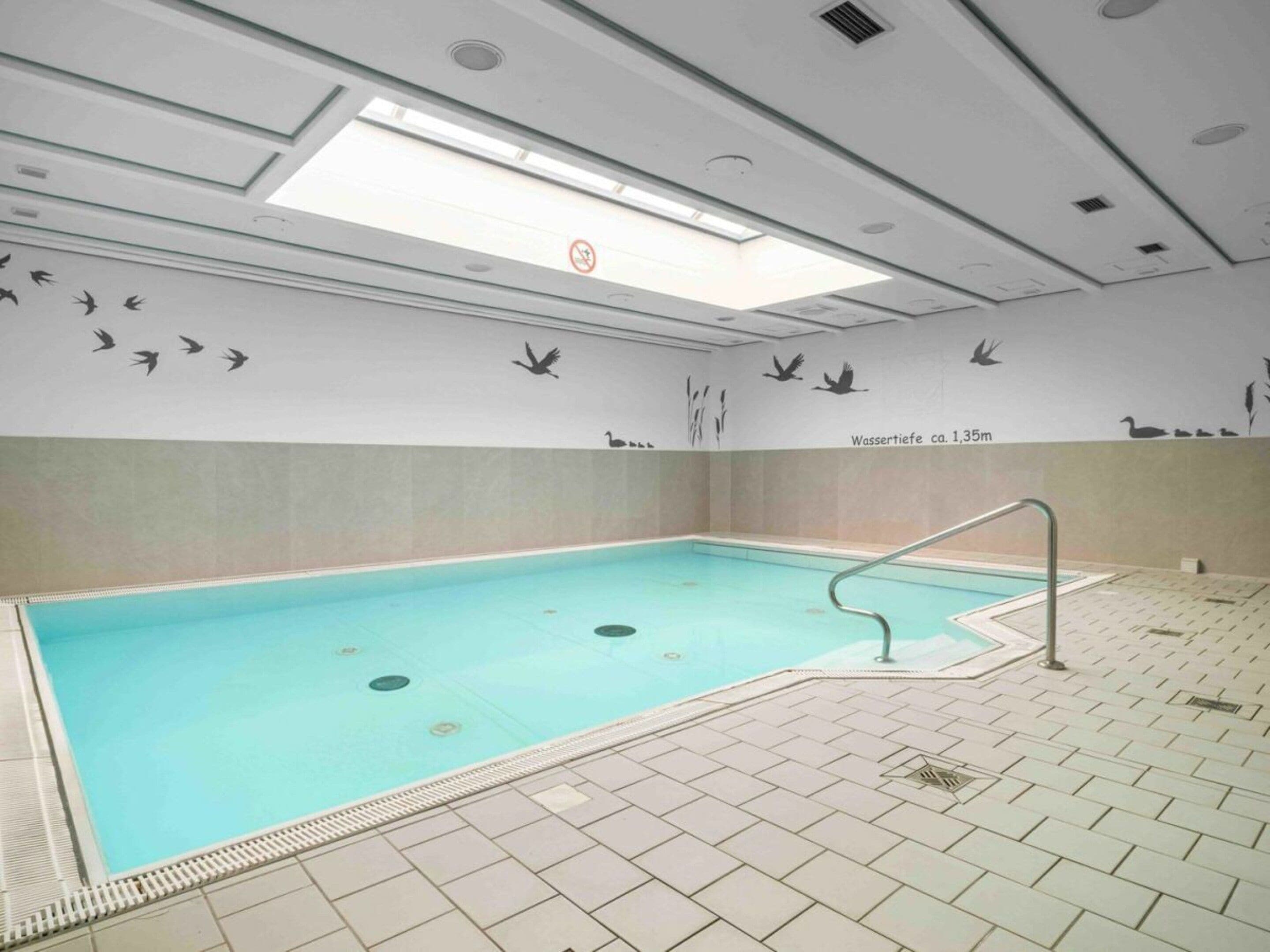 An indoor swimming pool with a tiled floor and a ceiling with skylights.