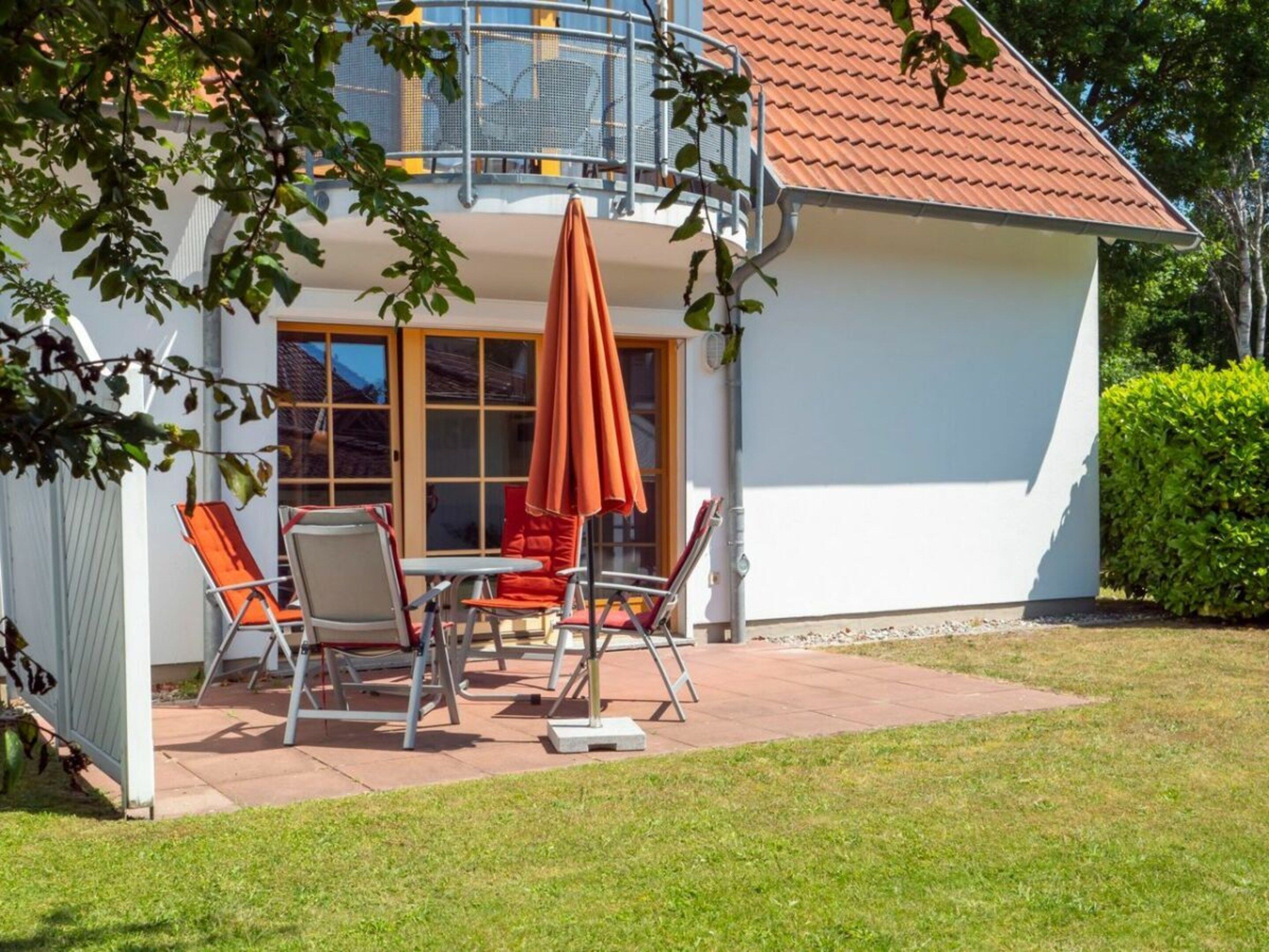 A house with a balcony, a patio with a table and chairs, and a covered area with an umbrella.